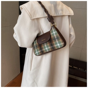 Close-up of a vintage plaid wool underarm bag with leather strap on a beige coat