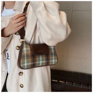 Close-up of green plaid wool underarm bag with brown leather flap and woven strap detail