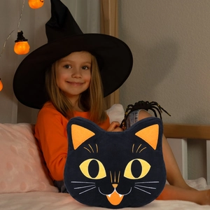 Halloween black cat plush pillow held by a girl in a festive holiday home setting