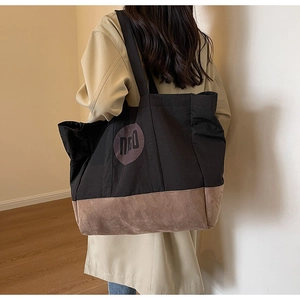 Vue détaillée d'un grand sac cabas en toile bicolore noir et marron porté à l'épaule