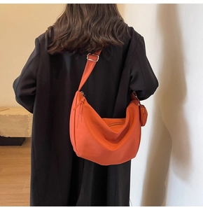Détail du sac hobo orange avec pochette ronde assortie sur un manteau noir élégant