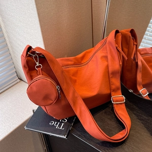 Grand sac à bandoulière en toile orange avec petit porte-monnaie rond sur un livre