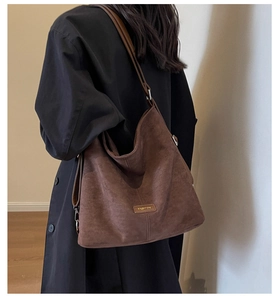 Detail of a large brown suede hobo bag with a gold metal logo and adjustable strap