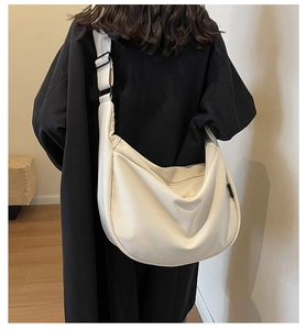 Gros plan du sac demi-lune en toile crème avec large bandoulière et texture tissu