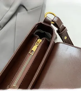 Detail of smooth gold zipper and d-ring on brown leather shoulder bag with grey lining