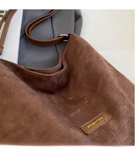 Detail of caramel brown suede hobo bag with gold metal fashion plaque and stitching