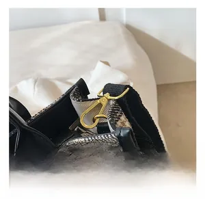Detailansicht des goldenen Metallhakens an einer karierten Tweed-Tasche mit Lederbesatz
