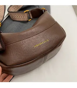 Gros plan d'un sac hobo en cuir marron foncé avec logo doré et bandoulière tissée