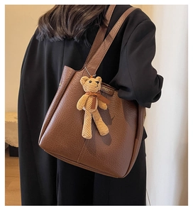 Detail of dark brown leather tote bag with knit bear charm and pebble texture finish