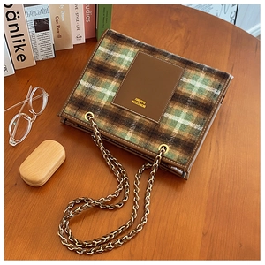 Detail of vintage green plaid wool bag with leather trim and gold chain on wooden desk
