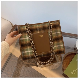 Detail of green and brown woolen plaid tote bag with gold chain strap and leather patch