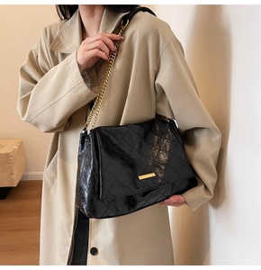 Gros plan sur la texture en cuir noir matelassé et chaîne dorée du sac à bandoulière