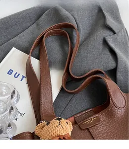 Detail of brown litchi pattern leather bucket bag with long straps and bear pendant