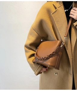 Détail d'un sac seau marron avec chaîne tressée décorative et pieds en métal doré