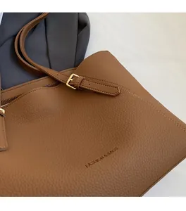 Détail du cabas en cuir marron à motif litchi avec boucle dorée et logo embossé