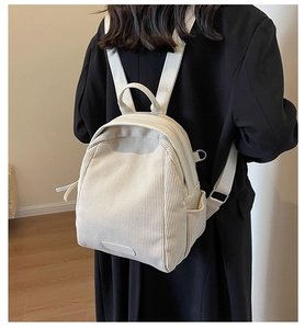 Detail of a cream corduroy backpack shown on model with textured fabric and side pockets