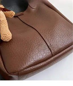 Close-up of brown litchi grain leather bucket bag with a knitted bear charm accessory