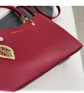 Close-up of deep red textured leather handbag with pearl and golden leaf charm detail