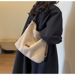 Close-up of beige suede shoulder bag with brown leather tag and fashion text