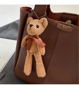 Detail of a handmade knitted brown bear charm attached to a brown textured leather bucket bag
