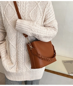 Détail du sac seau en cuir caramel avec poignée tressée et finitions métalliques dorées