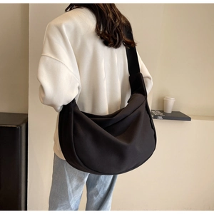 Détail d'un sac bandoulière en toile noire en forme de croissant porté par un mannequin