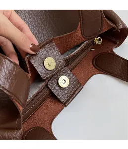 Close-up of golden magnetic clasp on brown lychee leather bag with herringbone lining