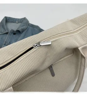 Detail of smooth silver zippers and corduroy texture on a beige tote bag