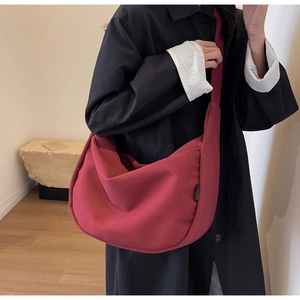 Détail du sac bandoulière en toile rouge foncé avec large sangle porté sur un manteau noir