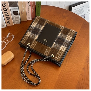 Macro view of brown plaid wool tote bag with golden chain strap on a wooden table