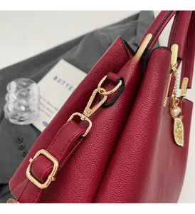 Detail of red lychee grain leather handbag with gold metal lock and pearl leaf charm