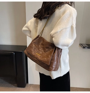 Détail d'un sac matelassé marron avec chaîne dorée sur un pull en maille blanc