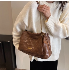 Détail d'un sac bandoulière marron matelassé avec chaîne dorée et boucle métallique chic