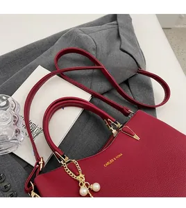 Detail of red lychee leather handbag with golden hardware and twin pearl pendant