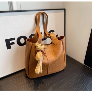 Detail of caramel brown litchi grain leather bucket bag with a cute knit bear charm