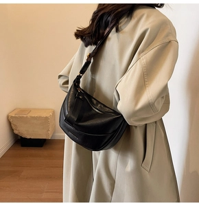 Détail du sac bandoulière demi-lune noir porté sur un mannequin en trench beige