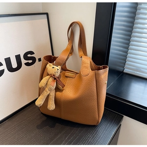 Detail of caramel leather bucket bag texture with a cute beige knitted bear charm