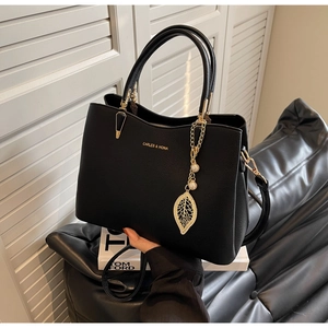 Detail of black pebbled leather handbag with gold leaf pearl charm and brand logo