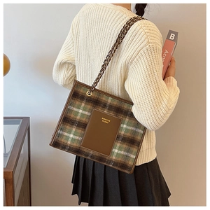 Detail of green plaid woolen tote bag with chain strap and leather logo patch on a model