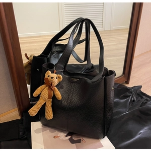Detail of black pebbled leather tote bag with gold label and brown knit bear charm