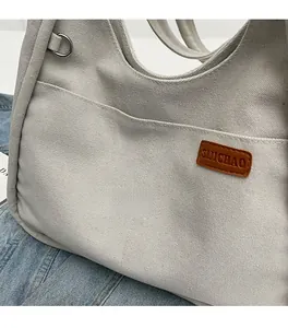 Detail of off-white canvas tote showing brown leather logo tag and textured fabric finish
