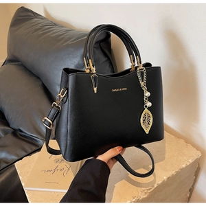 Detail of black pebbled leather handbag with gold pearl leaf charm on stone base