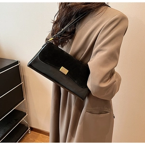 Detail of a black rectangular underarm bag featuring a matte flap and gold metal clasp
