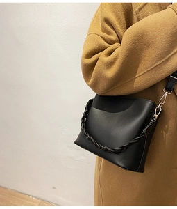 Détail d'un sac seau en cuir noir avec chaîne tressée et crochets dorés sur un mannequin