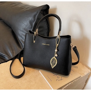 Detail of black lychee grain handbag with gold lettering and pearl leaf pendant