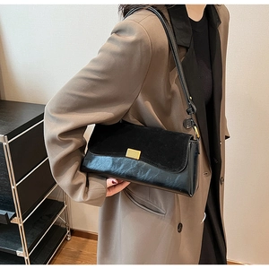 Detailed view of black underarm bag with matte suede flap and gold buckle on brown blazer