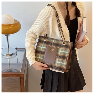 Detail of green and brown plaid tote bag with leather pocket and gold chain strap