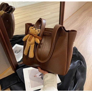 Detail of dark brown pebble leather tote bag with knitted bear charm and shoulder strap