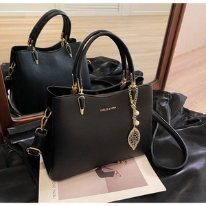 Close-up of black lychee grain leather handbag with gold leaf and pearl charms