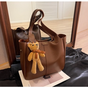 Detail of vintage brown leather tote bag featuring a gold metal tag and bear charm